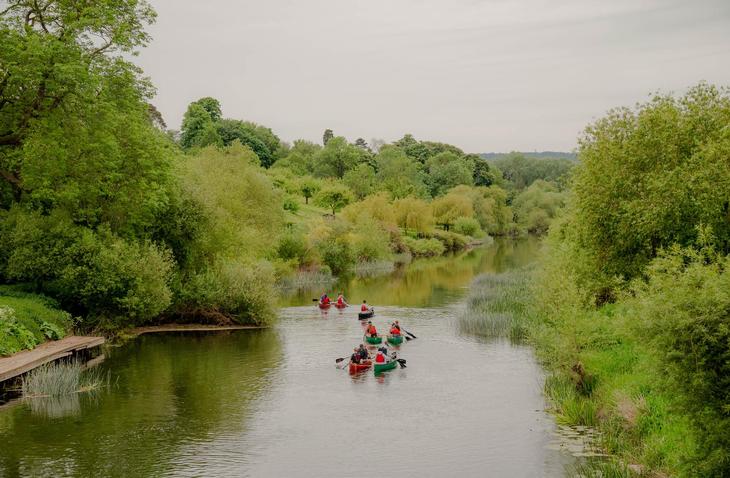 A peaceful scene of students canoeing along a slow running river amongst wildlife