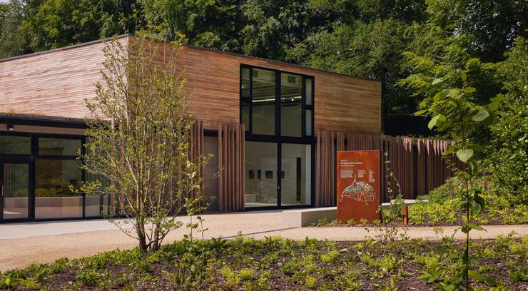 Photo shows Goodwood Art Foundation building clad in modern wood with dark window frames set in a leafy setting