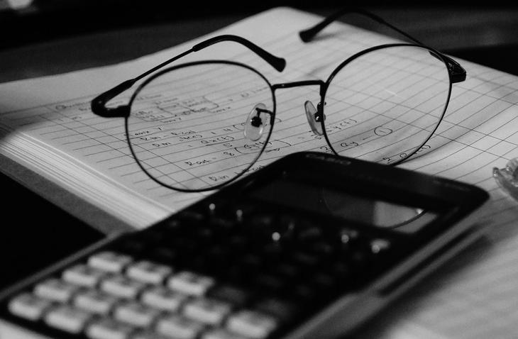 Scientific calculator on desk with of glasses and notebook showing calculations